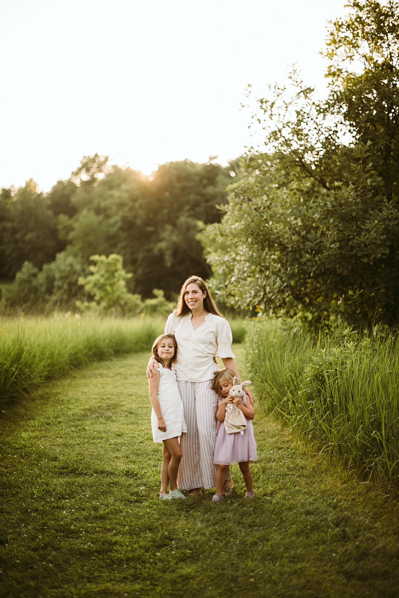 A family laughing together in a sunlit field of wildflowers during golden hour. Madison Wisconsin Photographer, Lake Mills Family Photos, family photo session