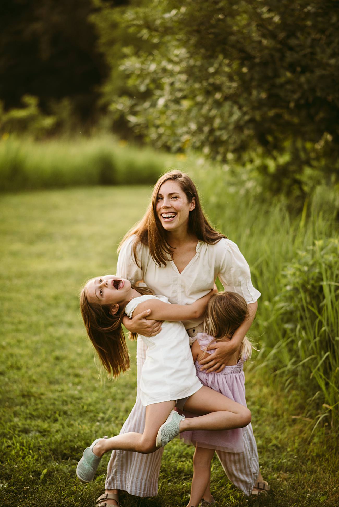 A family laughing together in a sunlit field of wildflowers during golden hour. Madison Wisconsin Photographer, Lake Mills Family Photos, family photo session